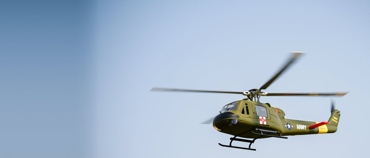 FLYWING UH-1 Huey scale RC helicopter in green Army paint flying against a clear sky